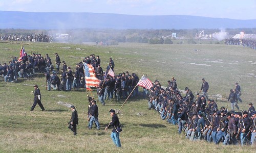 A long line of re-enactors in navy blue uniforms, carrying United States flags.