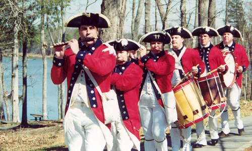Soldiers in colonial uniforms marching with musical instruments