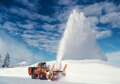 Snow plow shoots snow into the air and off of a road