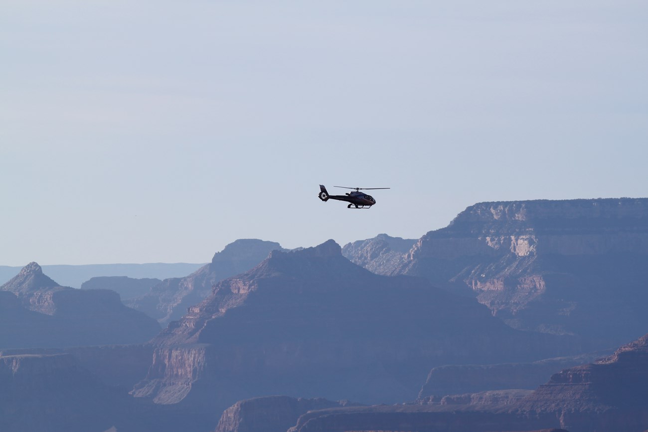 Dramatic buttes frame this view of a helicopter in flight at Grand Canyon National Park.