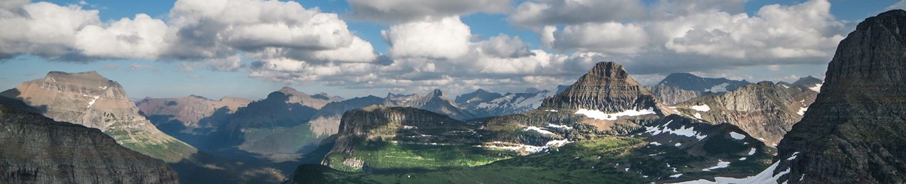 an aerial view of mountains with patchy snow under a partly cloudy sky