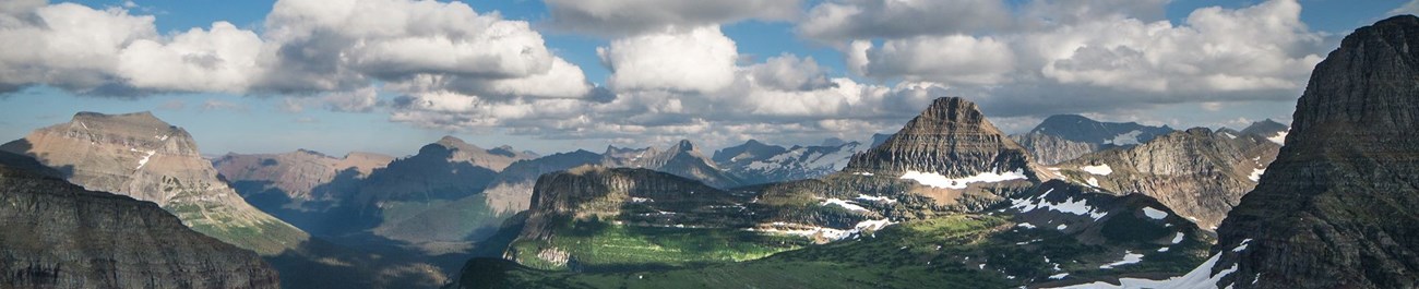 Glacier National Park an aerial view of mountains with patchy snow under a partly cloudy sky