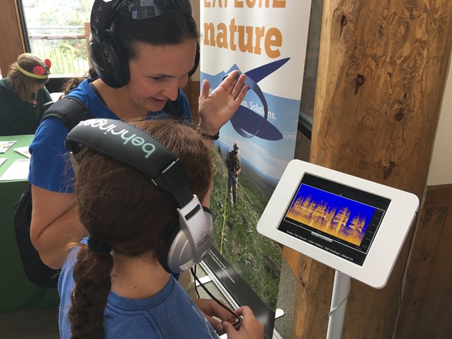 A mother and daughter stand before an ipad displaying spectrograms and play Guess That Sound, an educational game.