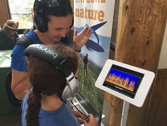 Mother and daughter test their skills in identifying sounds in Guess That Sound, an educational listening game. A mother and daughter stand before an ipad displaying spectrograms and play Guess That Sound, an educational game.