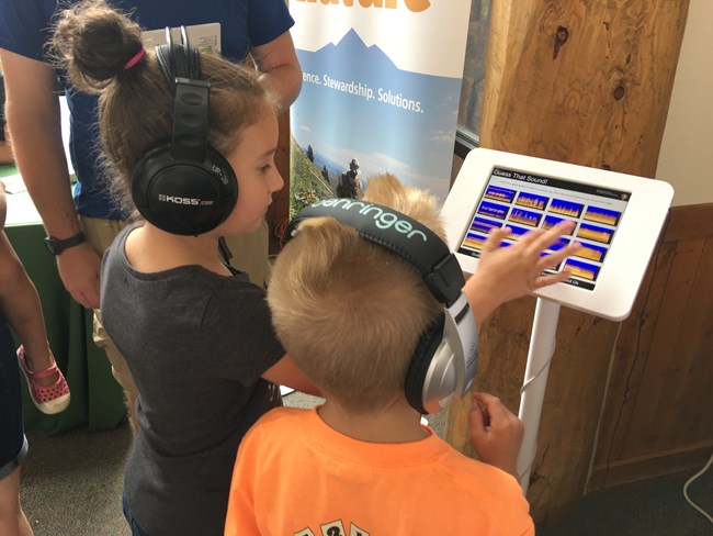 Rear view of two children interacting with a touch screen displaying spectrograms.