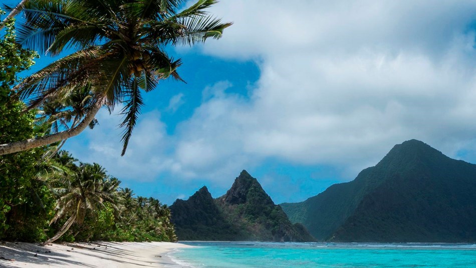 Landscape scene of tropical beach with palm trees, white sand and mountains at National Park of American Samoa
