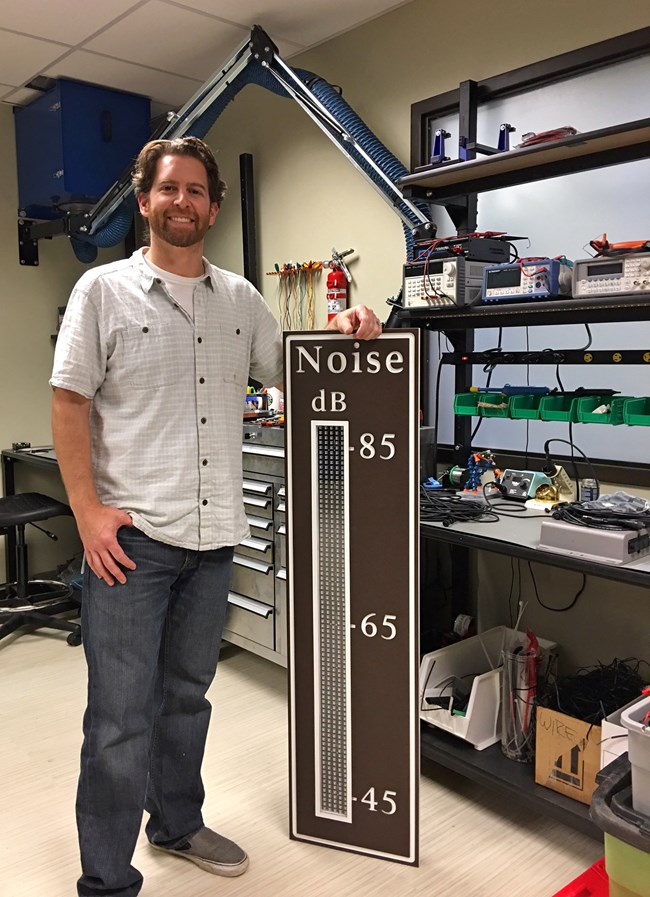 NPS acoustic technician Chris Garsha stands beside a newly created noise traffic display sign.