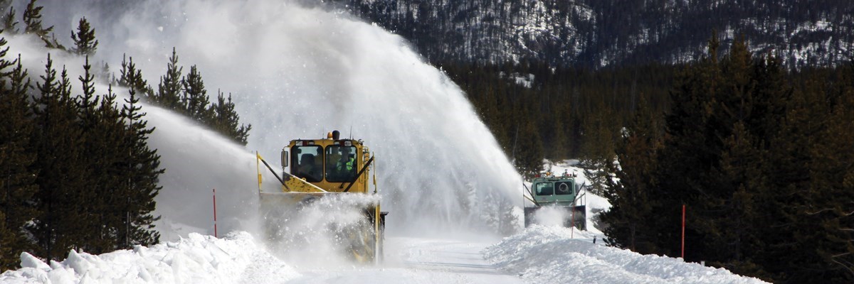 Frontal view of snow plows removing snow from road in a mountainous forested setting