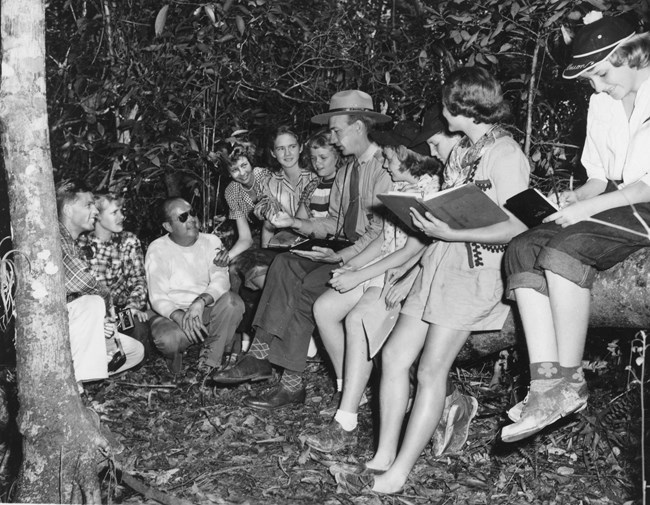 A park ranger reads from a book surrounded by Girl Scout troops