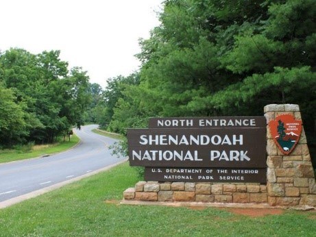 Entrance sign in grassy spot along the tree-lined roadway at Shenandoah National Park, which reads "North Entrance: Shenandoah National Park".