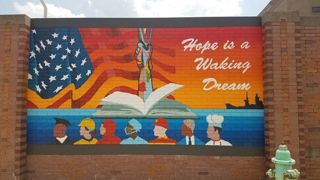Hope is a Waking Dream Colorful mural depicting people in profile under an American flag and clasped hands