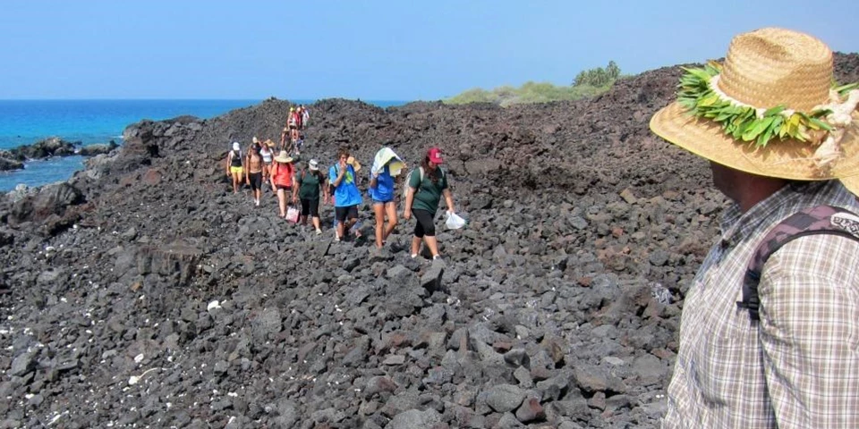 Ala Kahakai National Historic Trail Group of people hike through lava rocks near the ocean