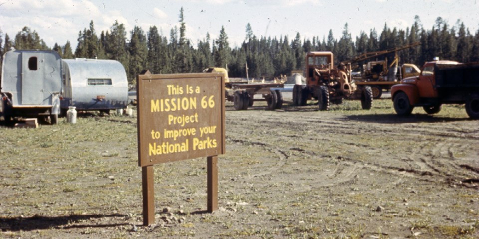 Sign for the Mission 66 project with vintage camping trailers and construction equipment behind it.