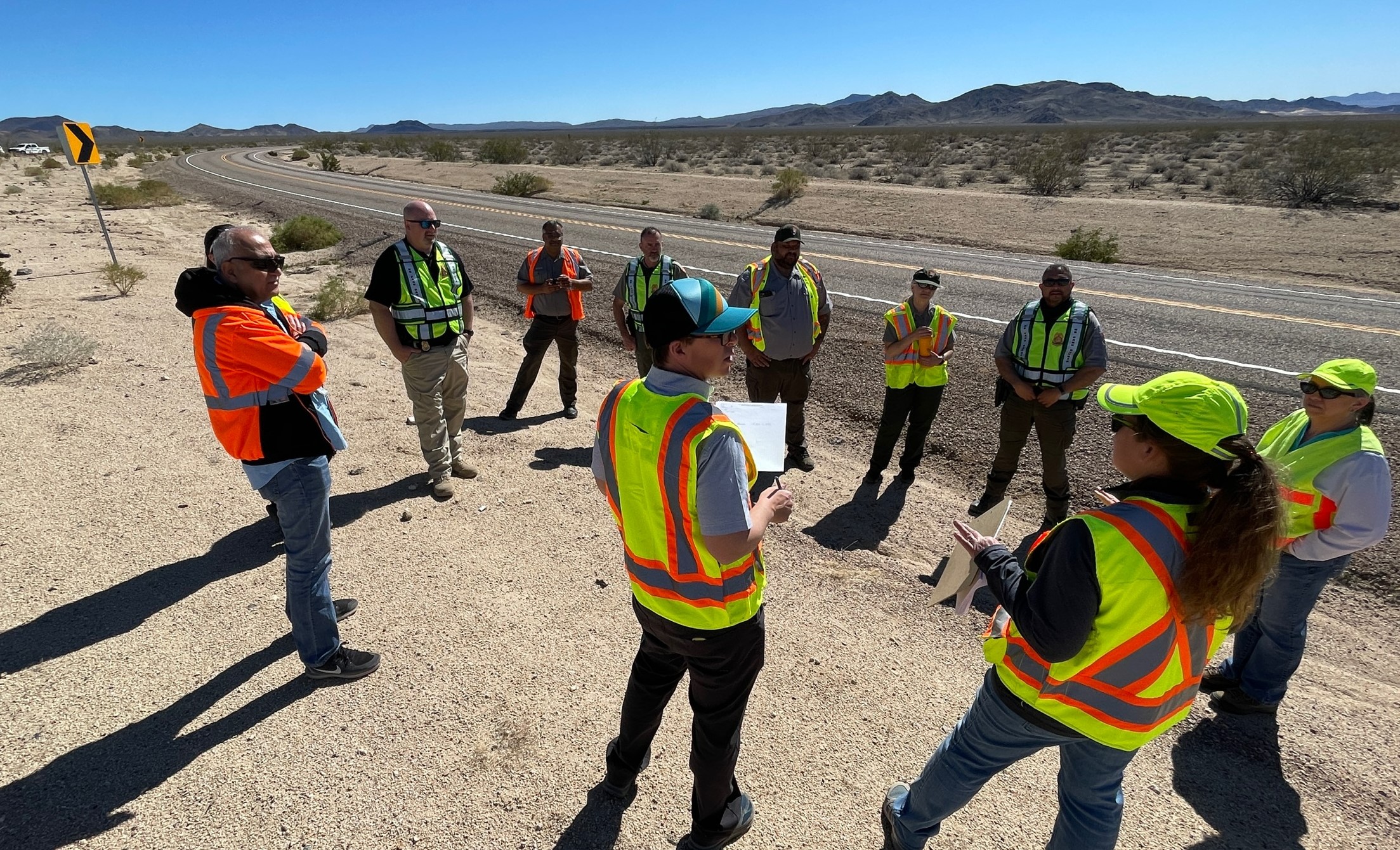 A group of people wearing safety vests, meeting on the side of a park road to discuss Transportation Safety