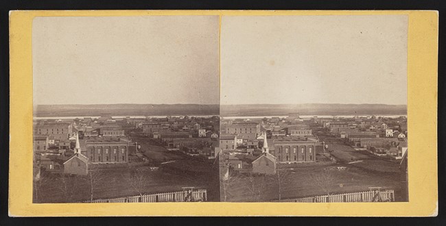 Farnam Street from hill west of city, c1868. Two story brick buildings, smaller frame buildings, dirt roads. Missouri River clearly visible and opposite bank empty.