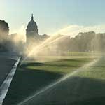 streams of irrigation water shoot over grass in front of US capitol