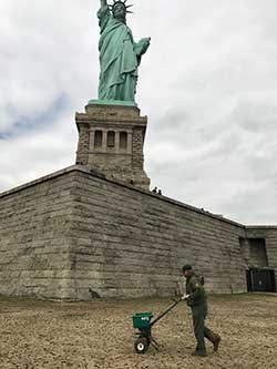 Person fertilizing STLI a person pushes a fertilizer bucket in front of the statue of liberty