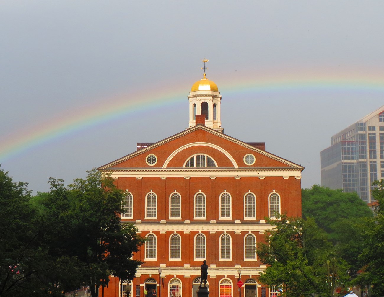 Four story brick building in with a rainbow hovering behind it