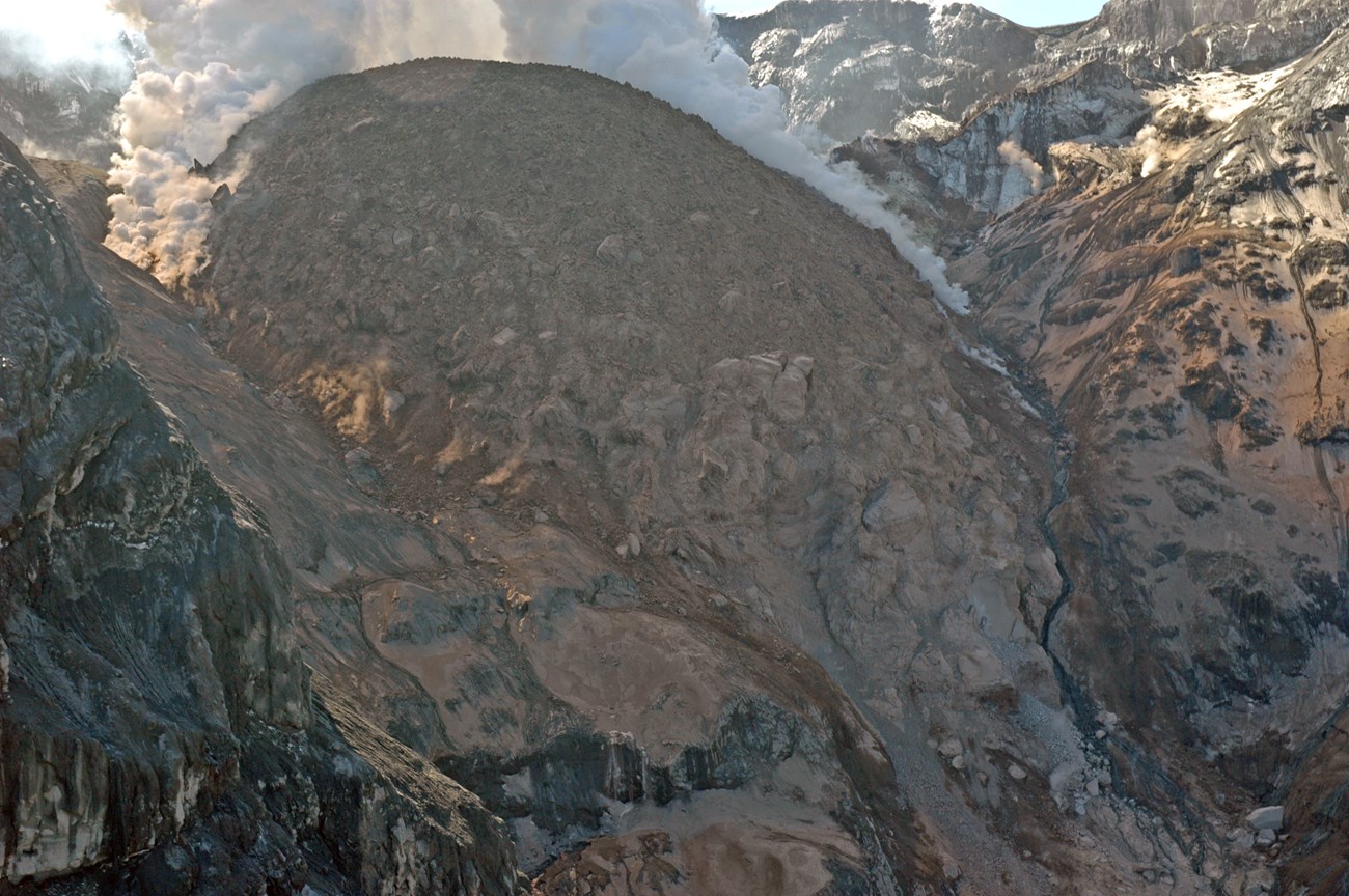 photo of a rocky dome-shaped feature with steam venting from the top and sides