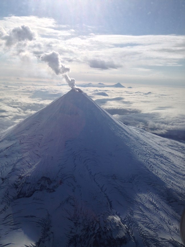 Aerial view of a conical volcanic peak with a steam plume