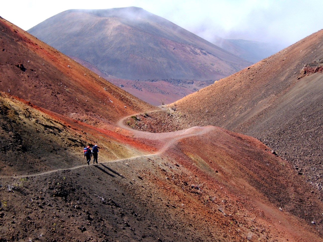 photo of hikers on a trail walking down a steep sided canyon of volcanic rocks and cinders