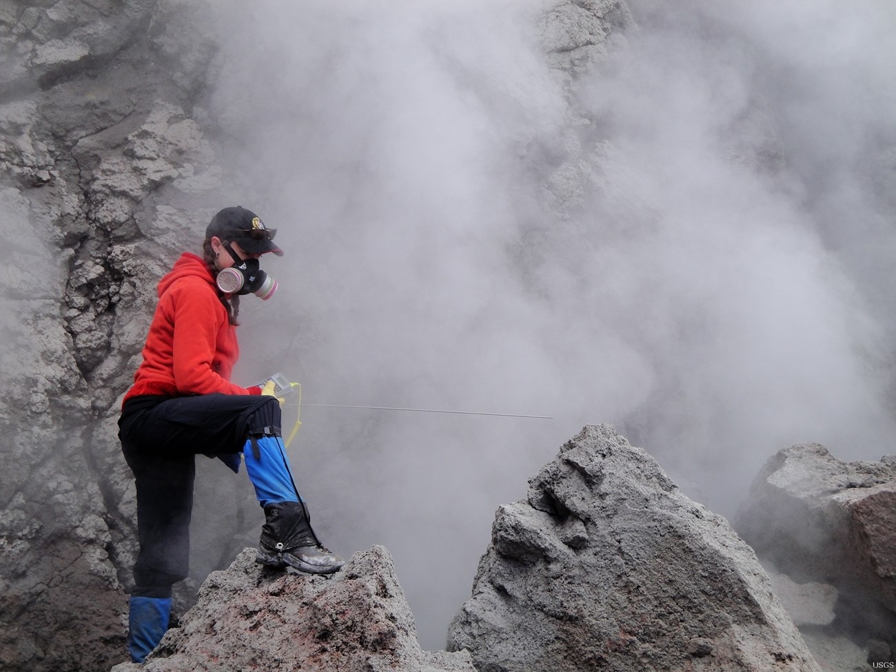 person with respirator on rocky slope near steam vent