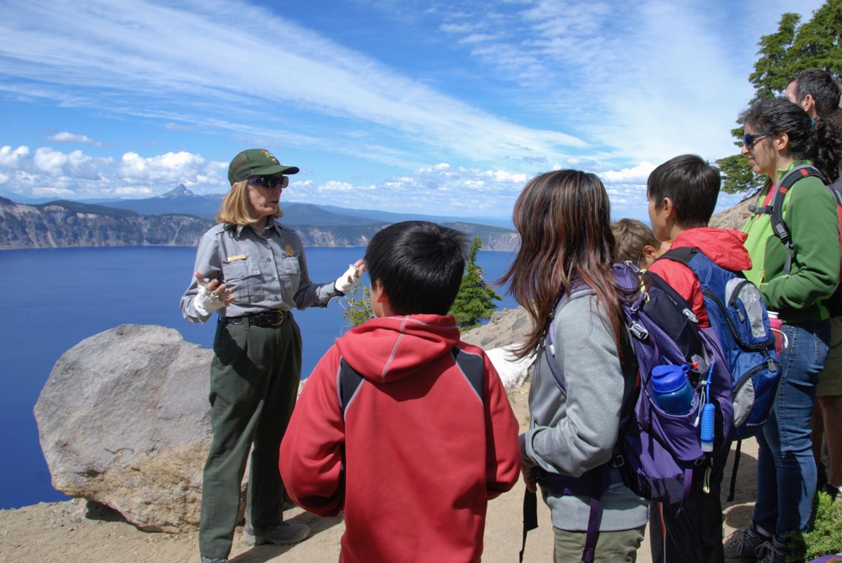 photo of a park ranger talking to a group of children on the rim of crater lake