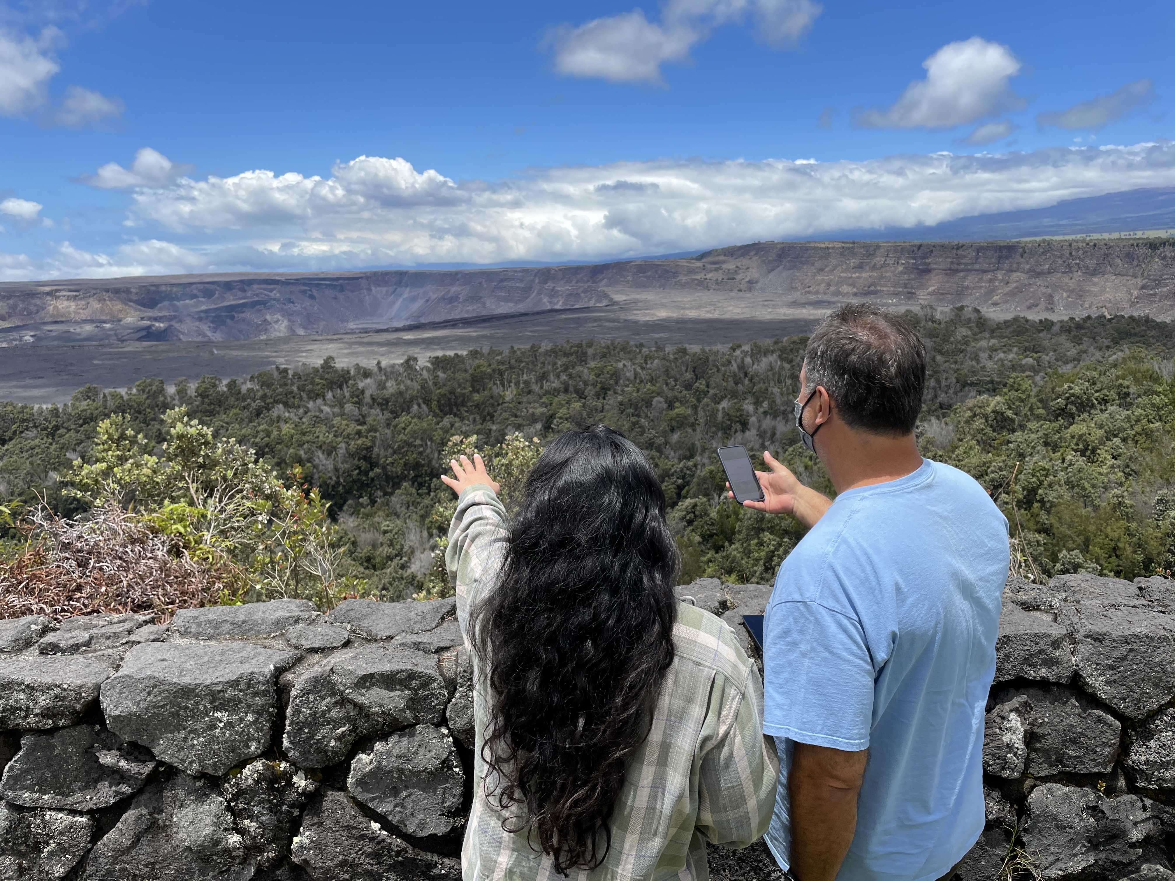 two visitors at volcanic crater using a mobile phone