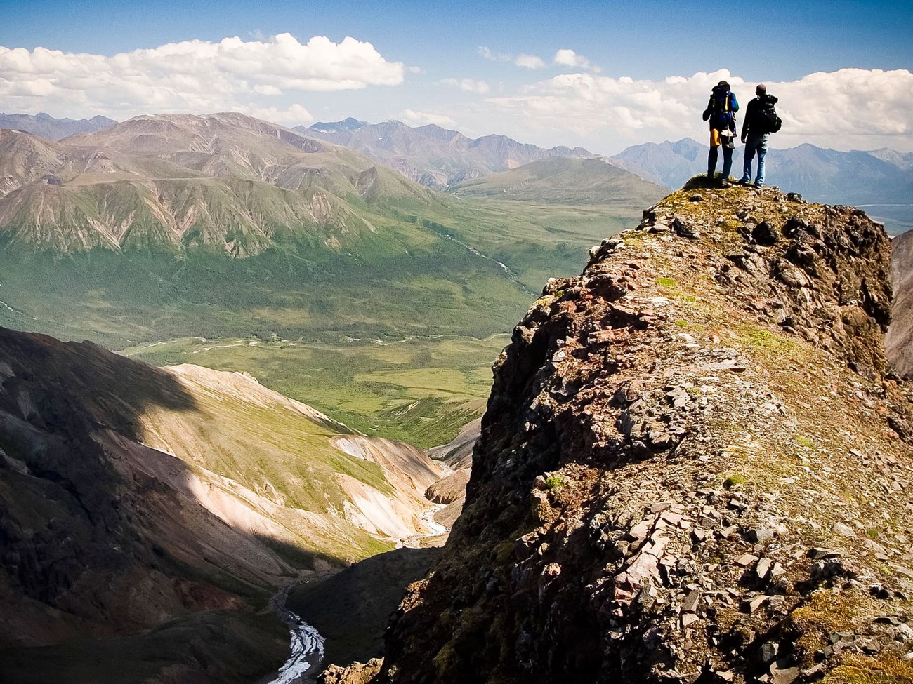 photo two hikers standing on a high volcanic bluff overlooking a valley with mountains in the distance