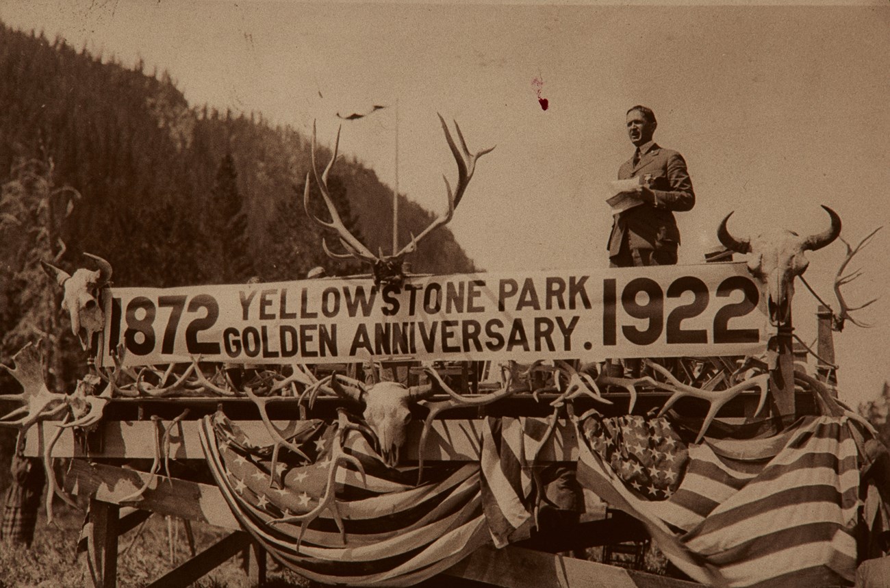 NPS Director Horace Alright givigin a speech from a stage with a sign celebrating the Yellowstone Golden Anniversary in 1922.