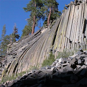 photo of a rock cliff with vertical columnar jointing and fallen rock pillars at the base