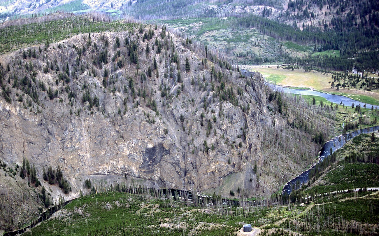photo of a rocky hillside viewed from above, a river flows in a valley below