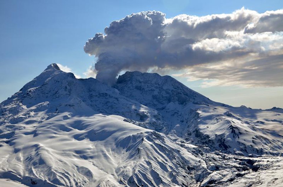 snow covered volcanic peak with steam and ash cloud