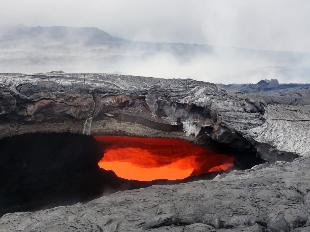 Photo of molten lava flowing beneath a hardened lava surface.