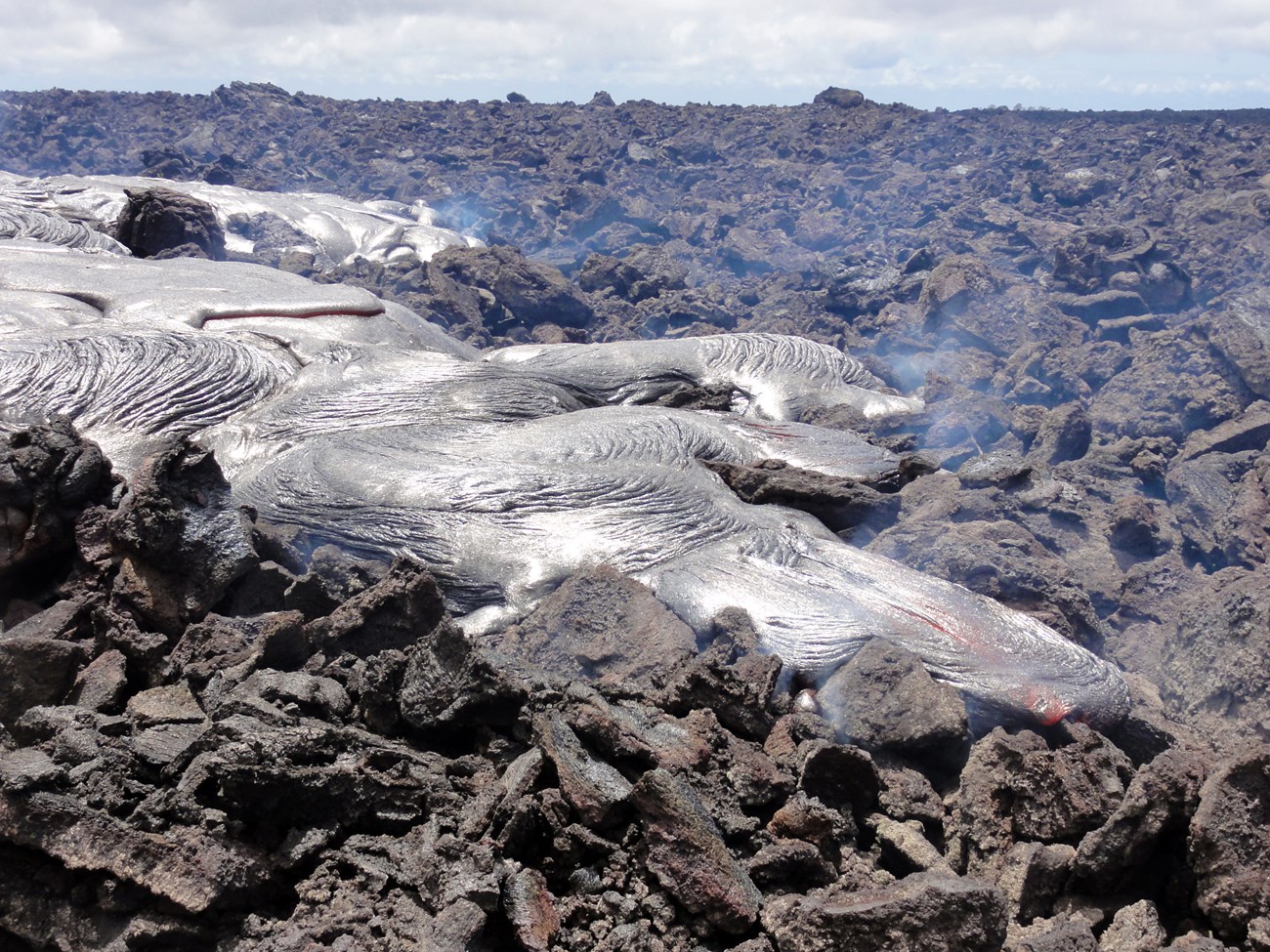 Photo of fresh lava flowing across a field of blocky broken lava.