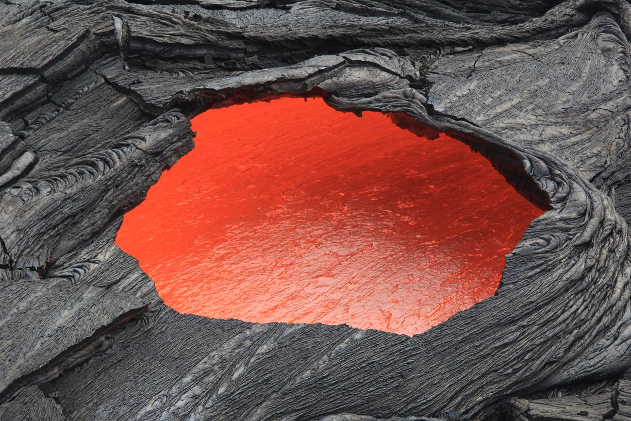 Photo of a hole in hardened surface lava where molten lava can be seen flowing beneath.