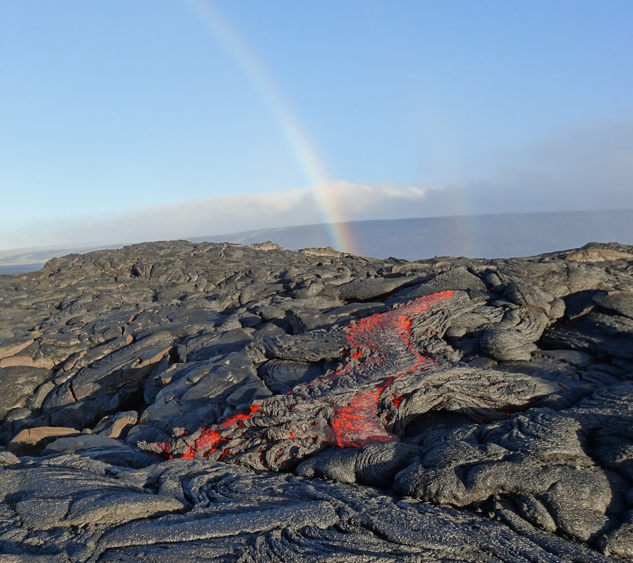 photo of a lava flow with molten rock and a rainbow