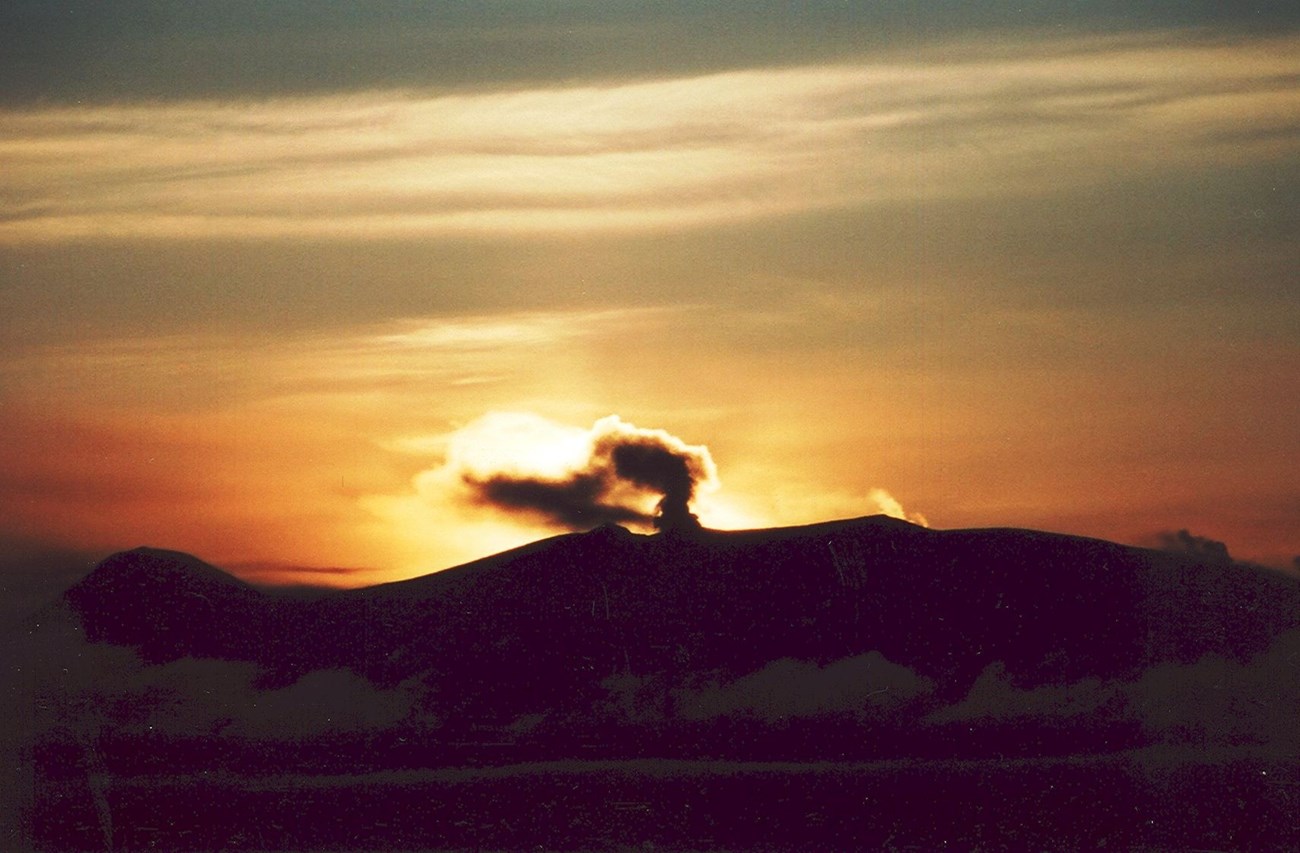 twilight silhouette of mountains with rising steam plume