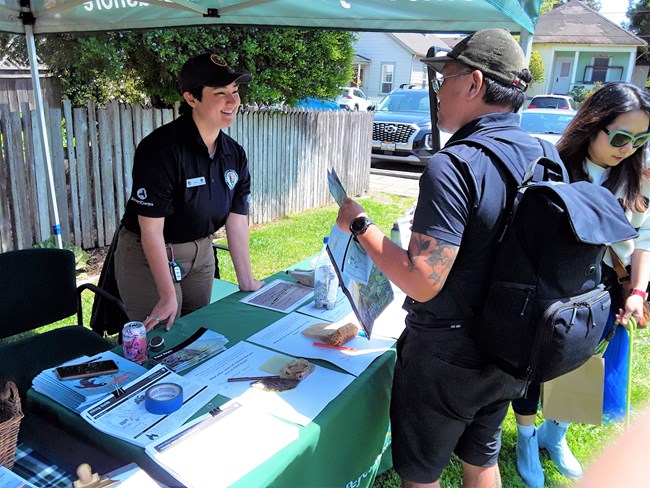 A photo of Keri, Community Volunteer Ambassador from Point Reyes National Seashore standing behind a table talking with park visitors.