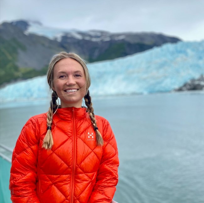 Brenna McGown wearing a red jacket in front of a glacier at Kenai Fjords National Park.