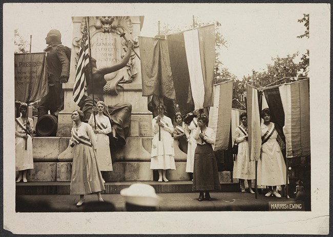 Photograph of five National Woman's Party members demonstrating, with banners, in front of the Lafayette Statue north of the White House in Washington.