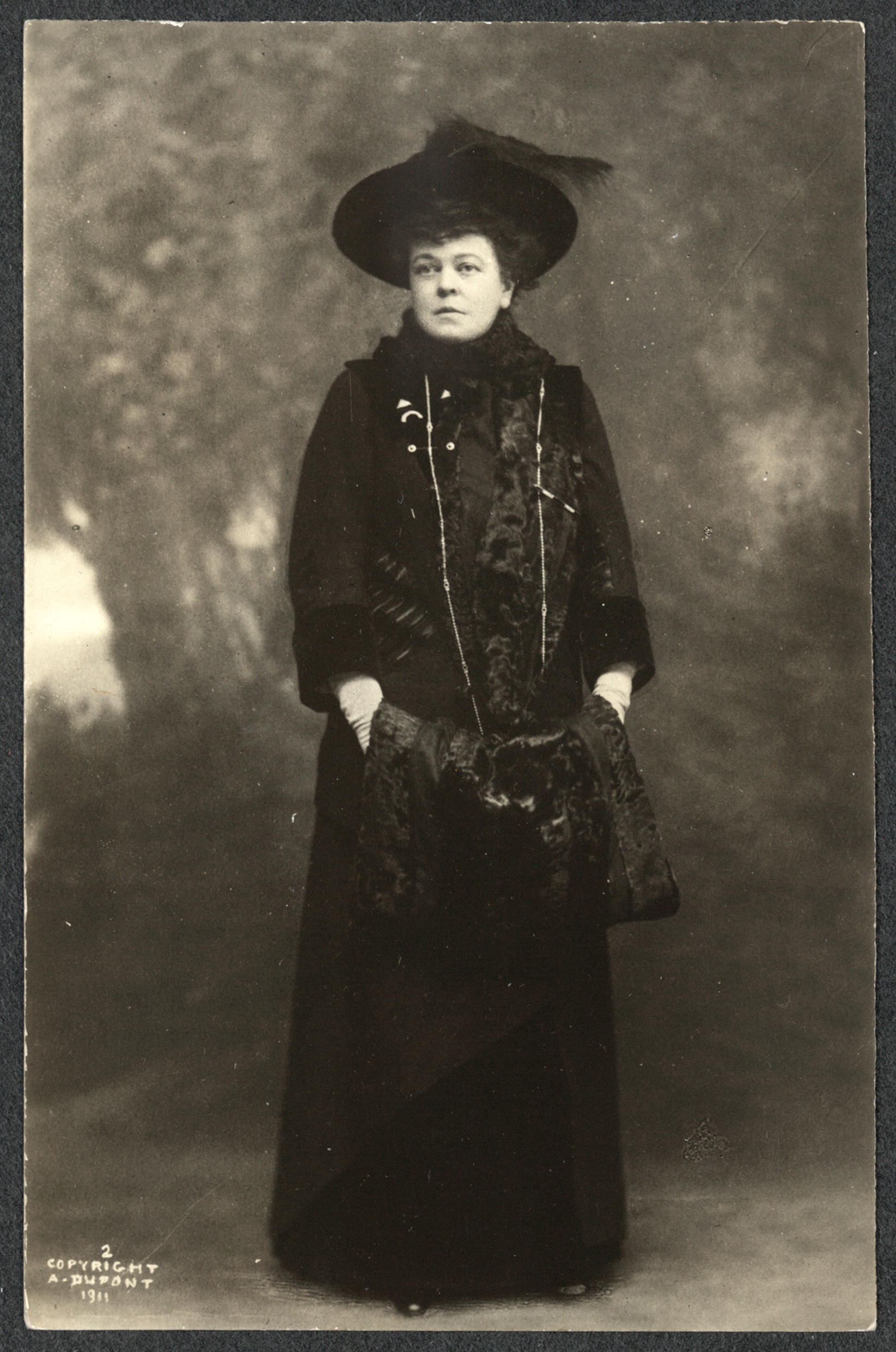 Full-length portrait of woman in fur-trimmed coat and muff.