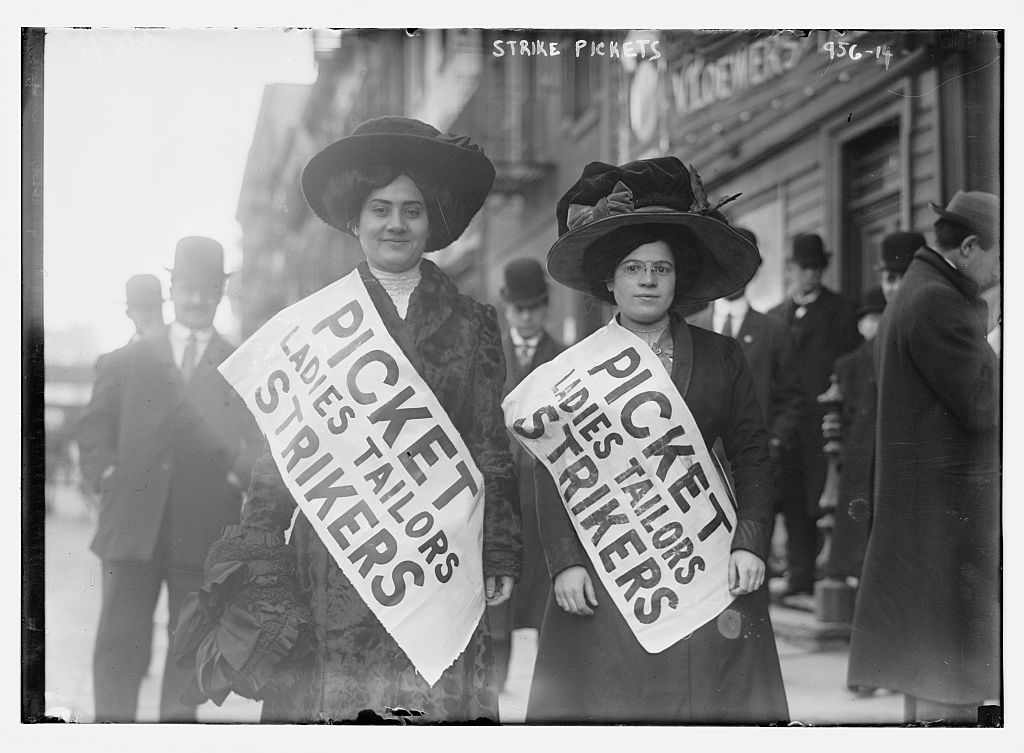 Two women face the camera wearing picket signs