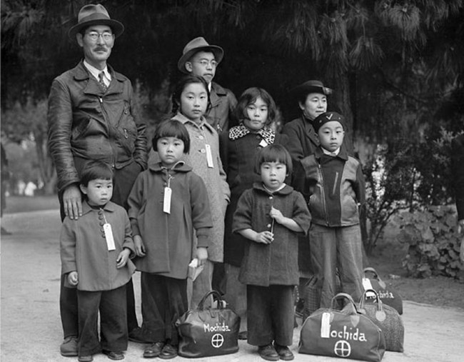 Japanese American family being relocated in 1942. Two adults, one teenage male, and 6 young children in the group.