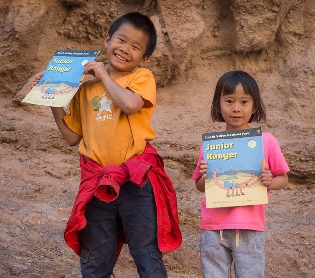 Junior Rangers smiling as they hold up their Death Valley Junior Ranger booklets