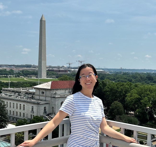 A woman stands in front of the Washington Monument on a rooftop