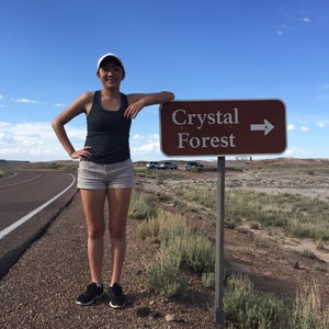 person leaning on a road sign that reads, "crystal forest"