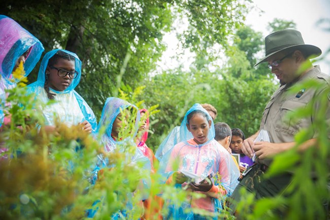 lt= boys and girls club members in rain coats with park ranger.