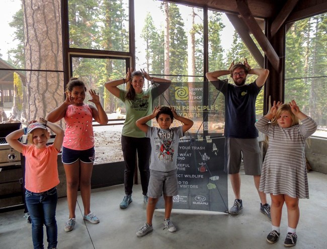 A group of Girl Scouts pose for a photo with Leave No Trace trainers Donielle and Aaron inside a picnic pavilion at the Volcano Adventure Camp