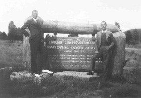 2 men standing with wooden entrance sign to CCC camp